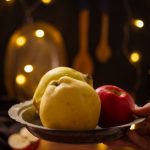A rustic composition featuring apples and quince illuminated by warm fairy lights indoors.