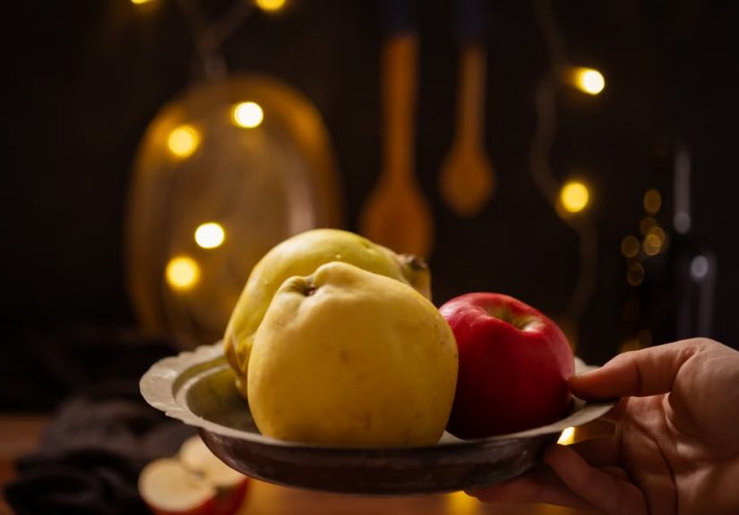 A rustic composition featuring apples and quince illuminated by warm fairy lights indoors.